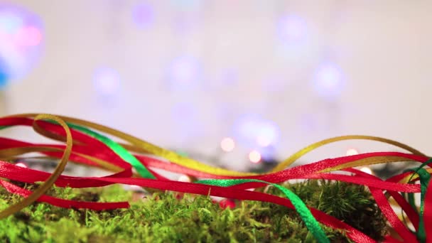 Barevné stuhy na zeleném mechu, vánoční stromeček dekorace s bokeh zpět. — Stock video