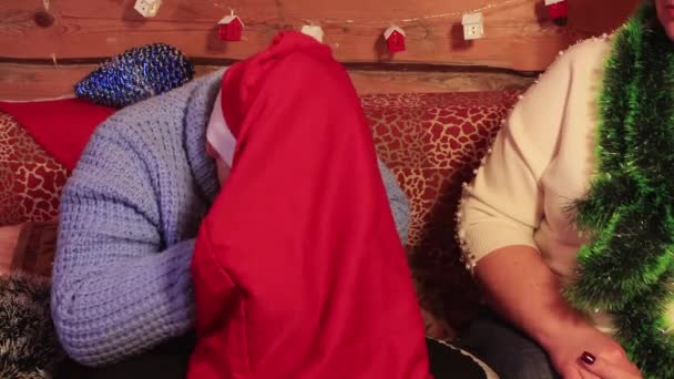 Um menino de chapéu vermelho de Papai Noel sobe em um saco de Natal. — Vídeo de Stock
