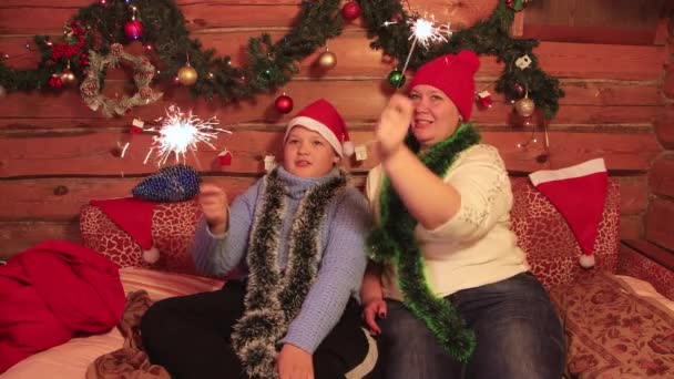 Chico y mamá en gorras rojas se divierten jugando con bengalas para Navidad. — Vídeos de Stock