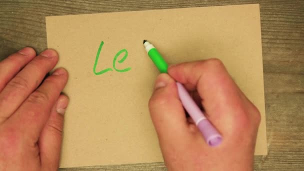 Une main d'homme écrit avec un stylo feutre vert sur une feuille de carton laissez-le montrer. — Video