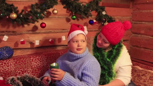 Un niño con una gorra roja de Santa Claus y una madre con una vela verde de Navidad. — Vídeos de Stock