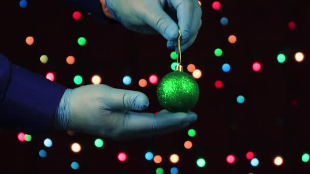 Les mains masculines, dans des gants médicaux, tiennent un jouet - une boule de Noël verte. — Video