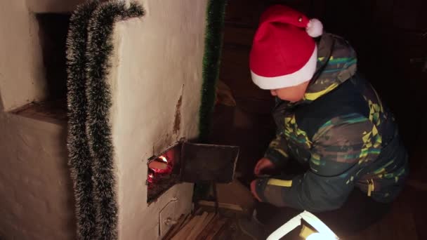 De jongen gooit het hout voorzichtig in de open brandende vuurkist.. — Stockvideo