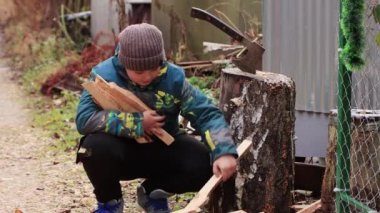 Elleriyle çömelmiş bir çocuk, bir kucak dolusu doğranmış sopa topluyor..