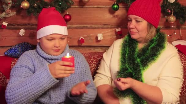 Pojken tar ett rött julljus från sin mor och blåser ut det. — Stockvideo