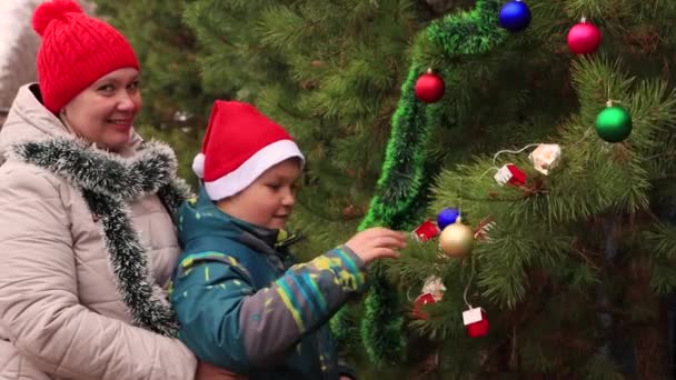 Moeder en zoon in de rode pet van de kerstman kijken naar feestelijke ballonnen — Stockvideo