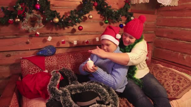 Mamá e hijo en gorras rojas sostienen una vela blanca de Navidad. — Vídeos de Stock