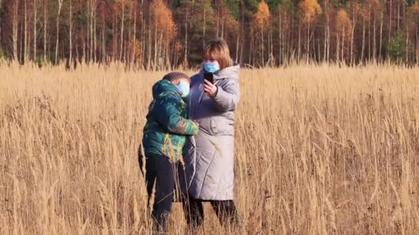 Máma a syn v maskách, ve vysoké trávě, jsou fotografováni po telefonu. — Stock video