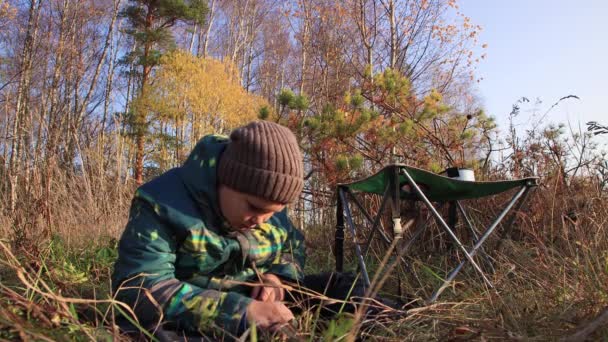 Chlapec v bundě sedí na trávě a dívá se na něco v ní. — Stock video