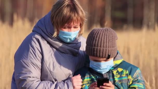 Мама з сином в масках, крупним планом перегляд фотографій на телефоні . — стокове відео