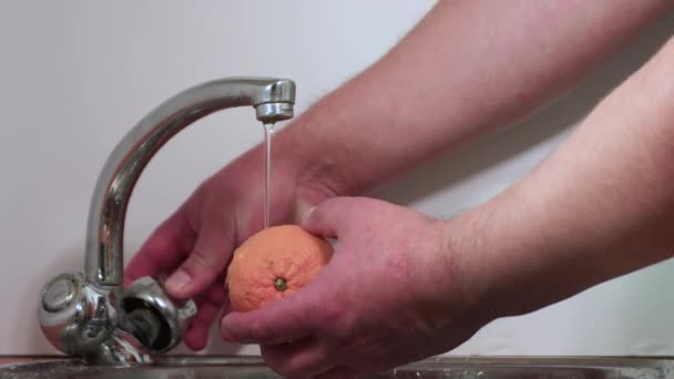 Mens hands wash orange tangerine under the stream with a quick motion. — Stock Video