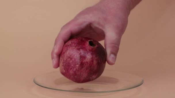 Mužská ruka pomalu umístí granátové jablko na skleněný talíř. — Stock video