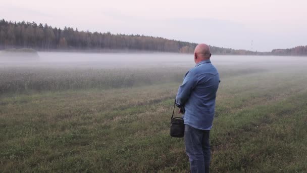 Un homme en jean se tient sur une prairie verte dans un brouillard épais. — Video