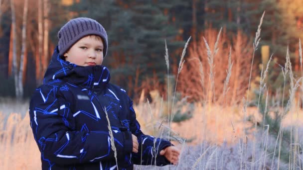 Портрет щасливого хлопчика в куртці і капелюсі, що грає з травою . — стокове відео
