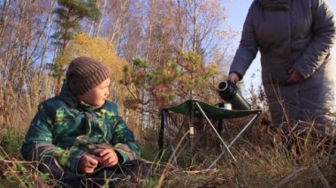 Çocuk çimenlerde oturur, anne. Arka plan termostan çay döker..