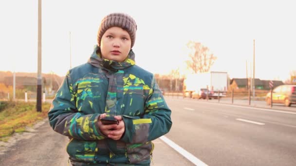 도로를 배경으로 한 한 남자 아이가 온라인으로 전화를 하고 있습니다.. — 비디오