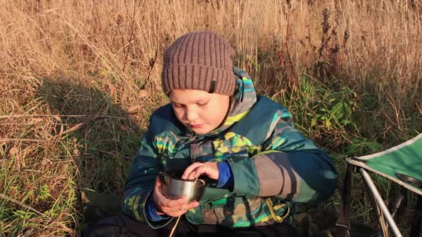 Un ragazzo in giacca seduto sull'erba, immergendo i biscotti nel tè e mangiando — Video Stock