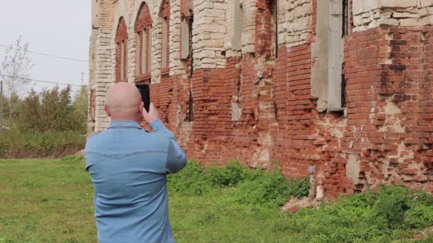 Ein Mann im Jeanshemd fotografiert eine zerstörte rote Backsteinmauer. — Stockvideo