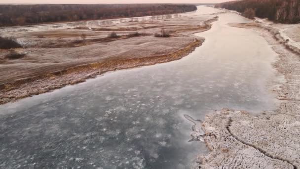 Aerial view of a snow-covered field at the edge of a frozen reservoir. — Stock Video