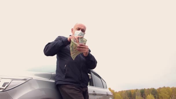 Un hombre de negocios con máscara está contando dólares contra el cielo. — Vídeos de Stock