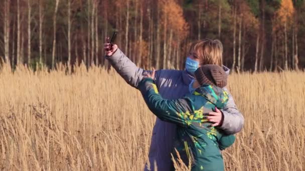 Μια γυναίκα με ένα αγόρι με μάσκες φωτογραφίζονται μαζί σε ένα smartphone — Αρχείο Βίντεο