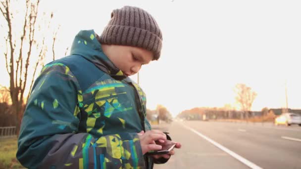 Contra o pano de fundo da rodovia, um menino usa a Internet online. — Vídeo de Stock