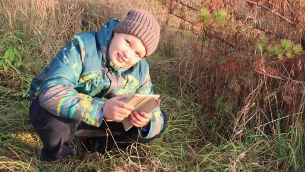Un garçon accroupi utilise Internet en ligne sur une tablette et regarde. — Video