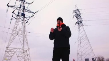 Sakallı beyaz bir adam, gri gökyüzüne karşı telsizle konuşuyor.. 