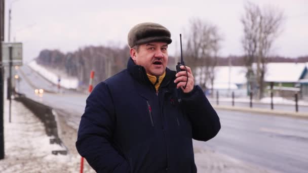 Caucásico joven hablando en un walkie-talkie primer plano, mirando a su alrededor. — Vídeos de Stock