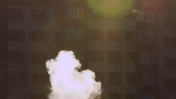 Vit rök stiger upp, en flervåningshus är ur fokus bakom — Stockvideo