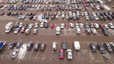 Cars are standing in straight rows in the parking lot, people are walking.