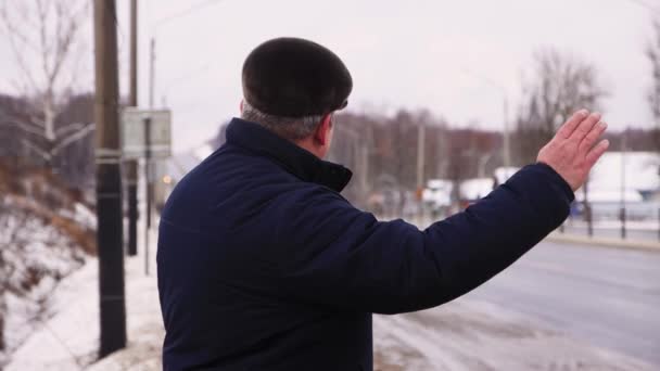 Egy férfi áll az út szélén, felemeli a kezét, megállítja az utat.. — Stock videók