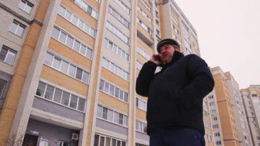 Bir adam bahçede duruyor, taksi bekliyor ve telefonda konuşuyor..