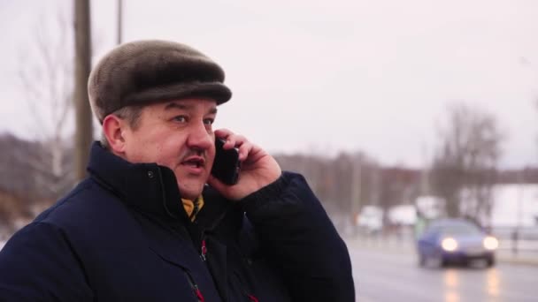 Een man die aan de kant van de weg staat spreekt energiek aan de telefoon. — Stockvideo