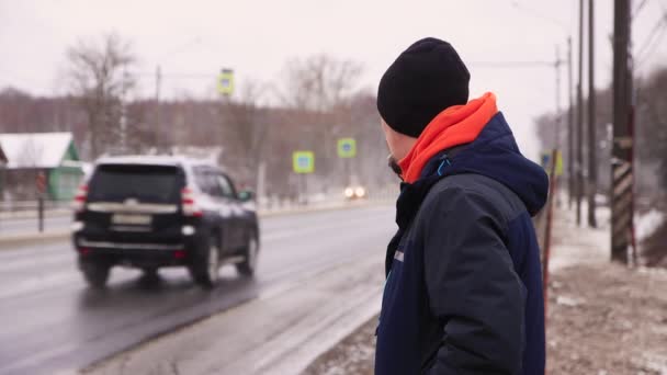 Un joven está de pie a un lado de la carretera esperando su transporte.. — Vídeos de Stock