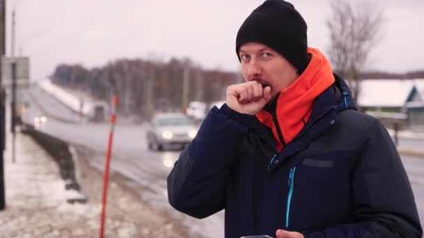 Sérieux jeune homme debout sur le bord de la route et se réchauffant les mains. — Video