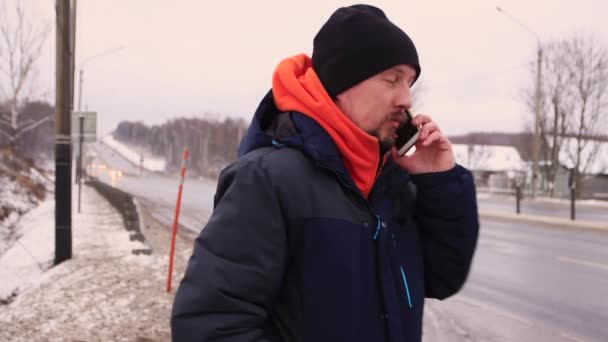 Un hombre parado a un lado de la carretera está hablando por teléfono y sonriendo. — Vídeos de Stock