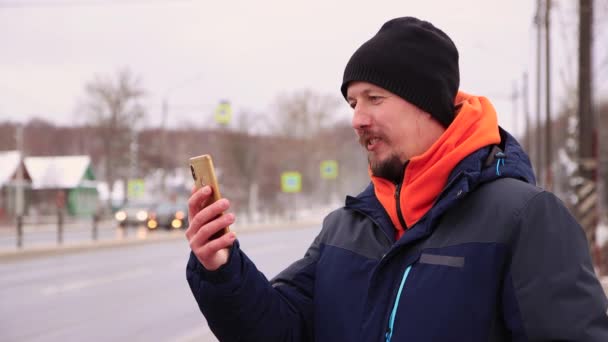 En ung man vid vägkanten pratar i telefon på nätet och skrattar — Stockvideo