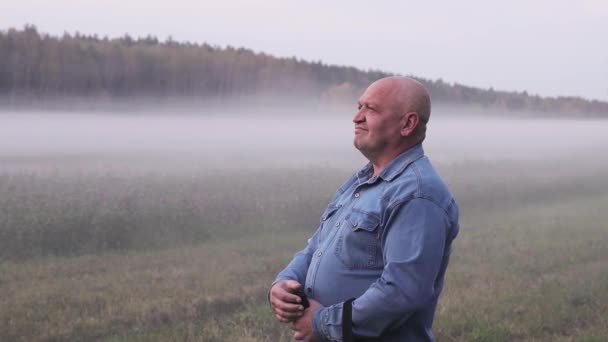 Un homme en chemise de denim se tient dans le brouillard épais et caresse sa tête chauve — Video