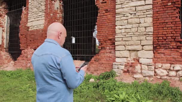 A man looks into the phone against the backdrop of ruins of white and red stone — Stock video