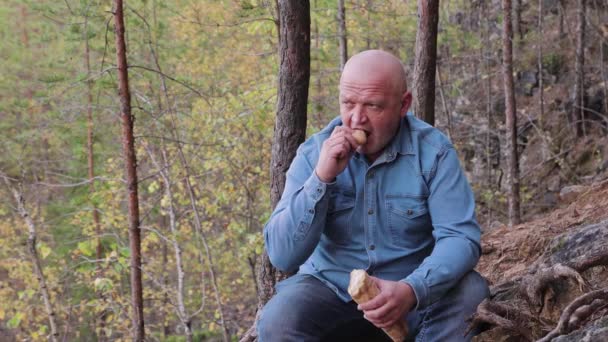 Primer plano de un hombre sentado en el borde de un acantilado comiendo una baguette. — Vídeo de stock