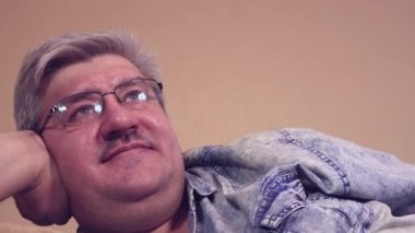Kanepede gözlüklü mutlu adam rahatça güler.,