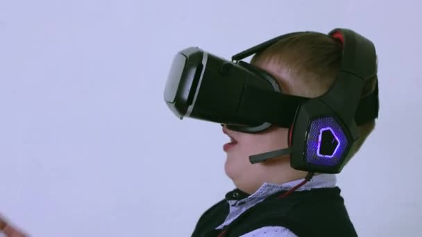 Un garçon dans un casque de réalité virtuelle et écouteurs rit beaucoup. — Video