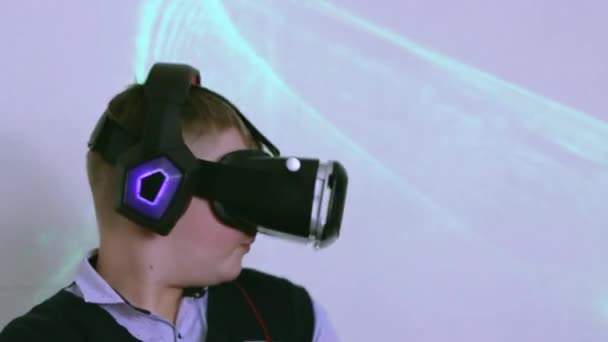 Un niño en un auricular de realidad virtual y auriculares está bailando de perfil. — Vídeos de Stock