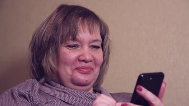 Счастливая женщина, держащая в руках смартфон, сидит дома на диване — стоковое видео
