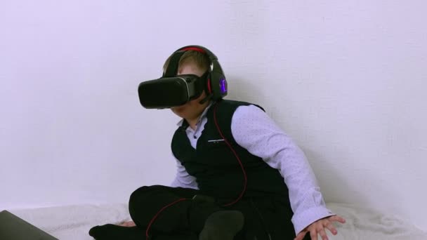 Un garçon dans un casque de réalité augmentée et écouteurs s'assoit et esquive — Video