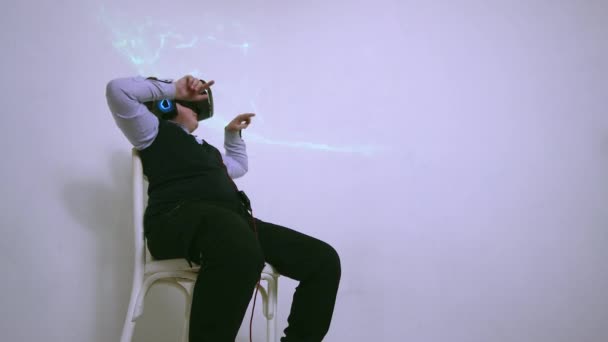 Egy fiú egy virtuális valóság headset és fejhallgató egy széken nyomja meg a gombokat — Stock videók