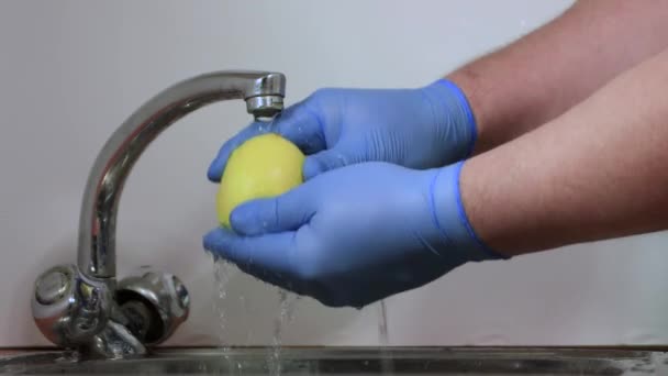 Las manos masculinas con guantes azules enjuagan bien el limón amarillo. — Vídeos de Stock