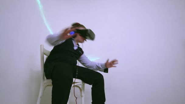 En pojke i en virtuell verklighet headset och hörlurar sitter på en stol lutar sig över — Stockvideo