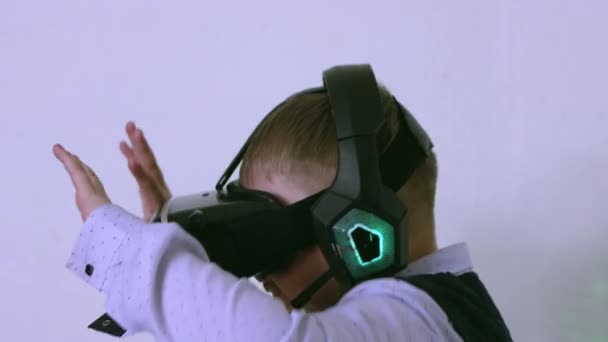 Un garçon dans un casque de réalité virtuelle et écouteurs se ferme avec ses mains — Video